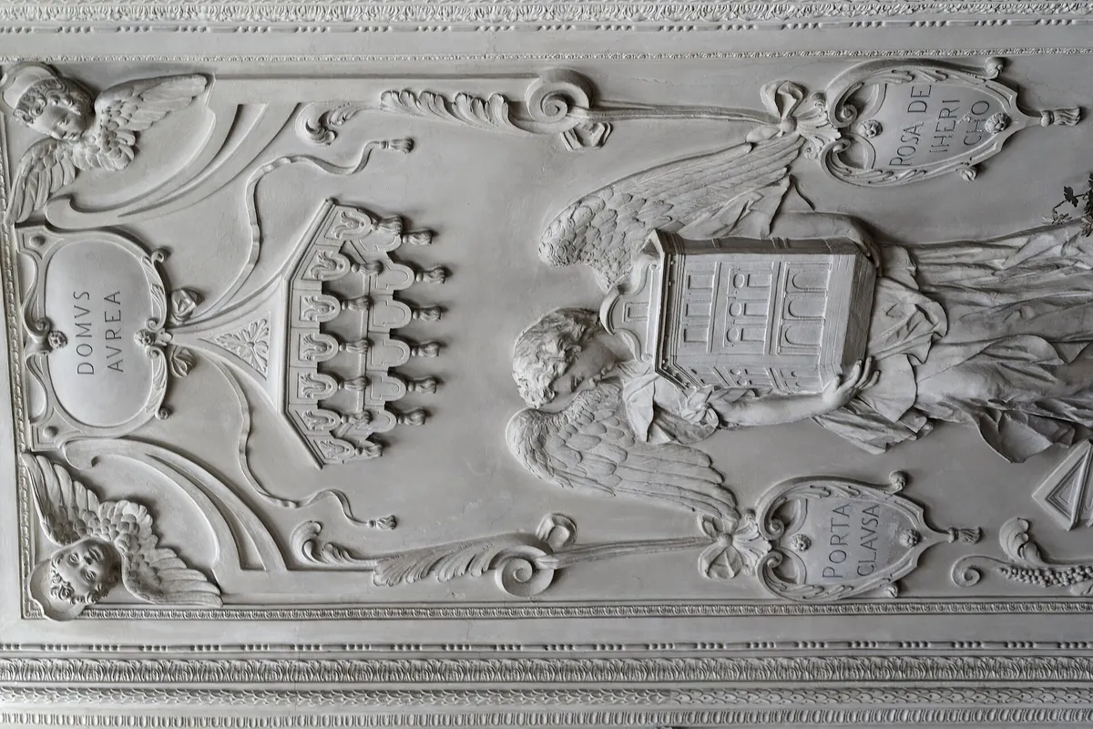A stucco panel in the chapel showing coats of arms, angels and ornament in white relief.
