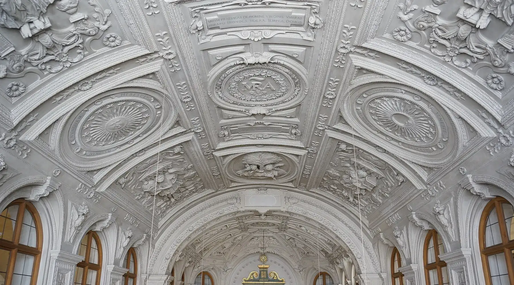 The vault of the court chapel covered in white stucco ribs, oval medallions and relief ornament, with arched windows below.